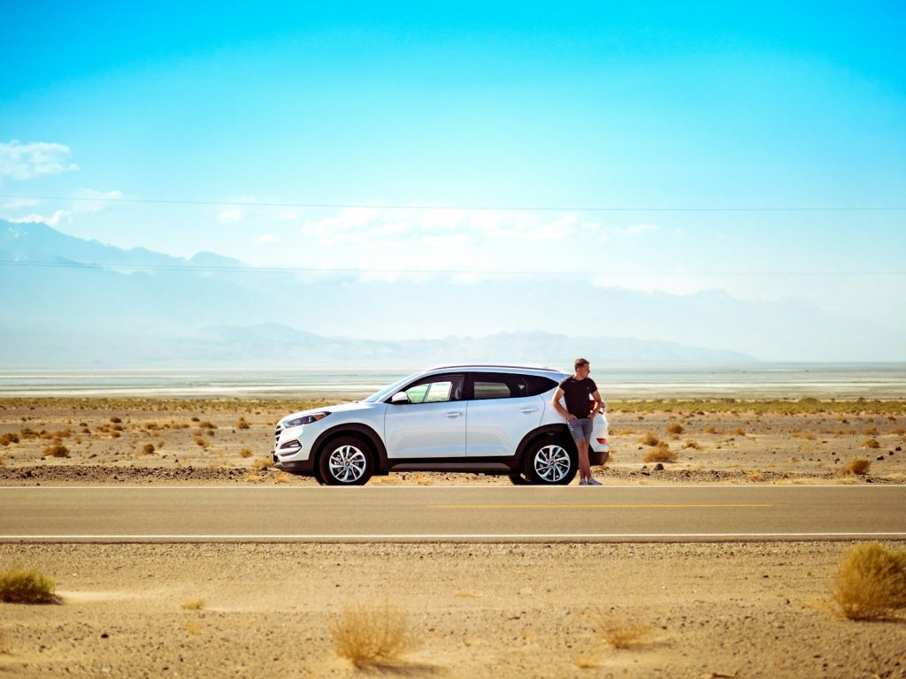 man standing beside his car in a road on summer 